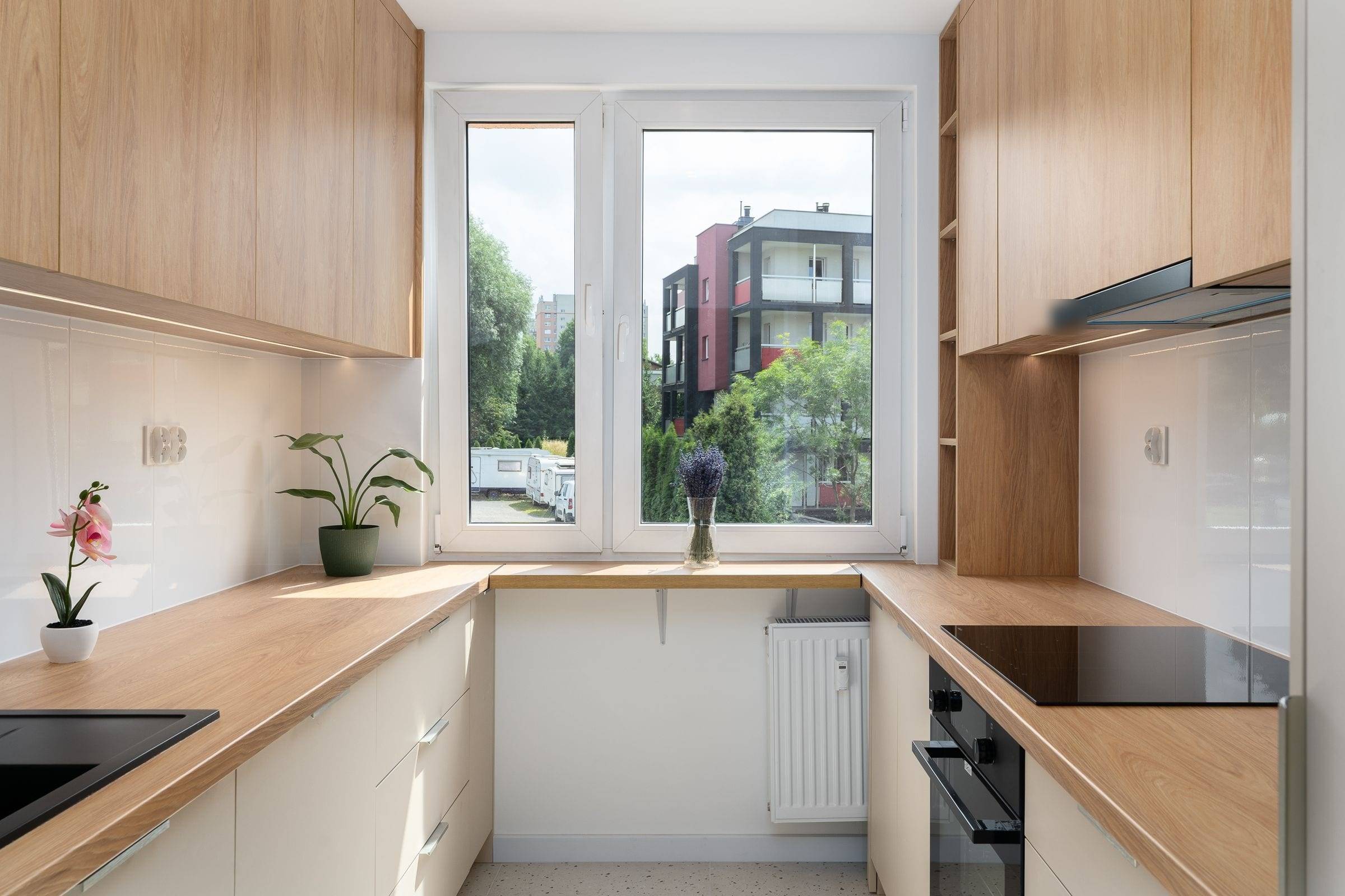 Cuisine en U rénovée autour d’une fenêtre, meubles hauts en chêne clair, bas crème et plans de travail effet chêne
