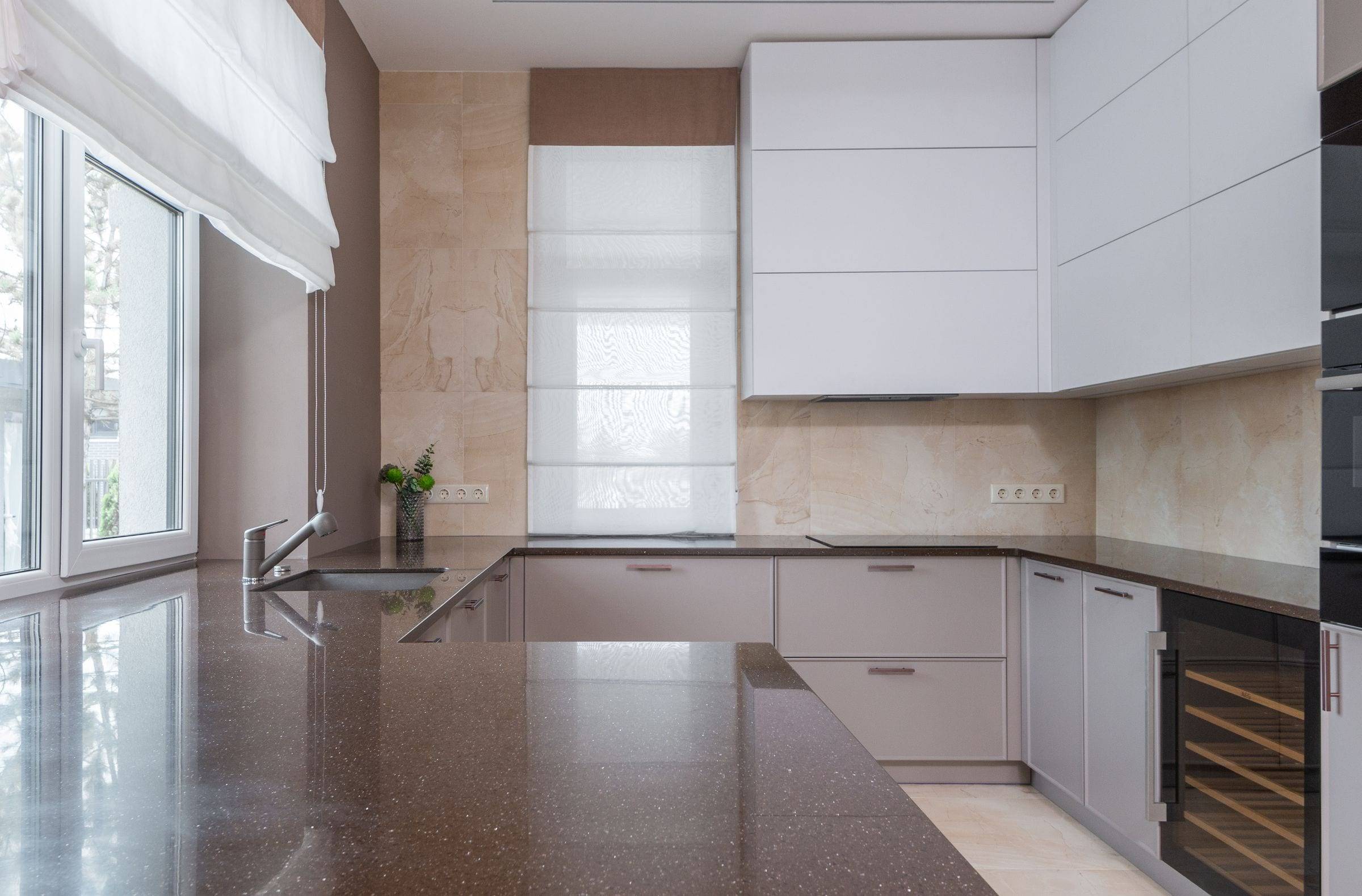 Cuisine en U aux façades taupe et blanches, plan de travail en quartz brun pailleté et évier sous plan