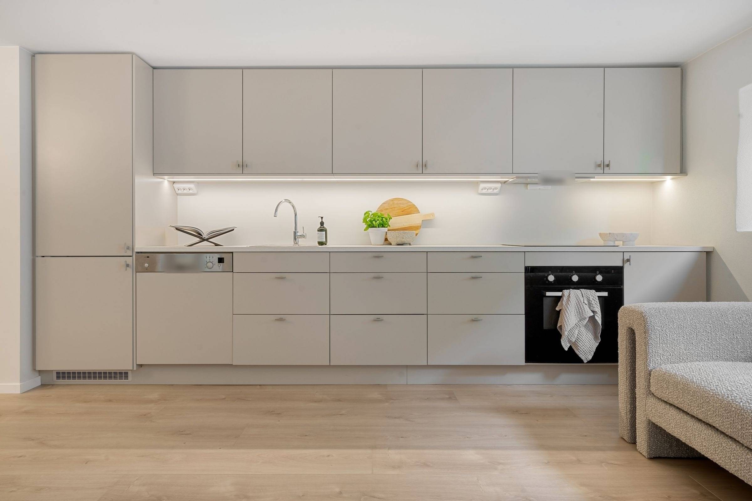 Cuisine linéaire beige mate avec meubles hauts, éclairage LED sous les meubles et colonne réfrigérateur