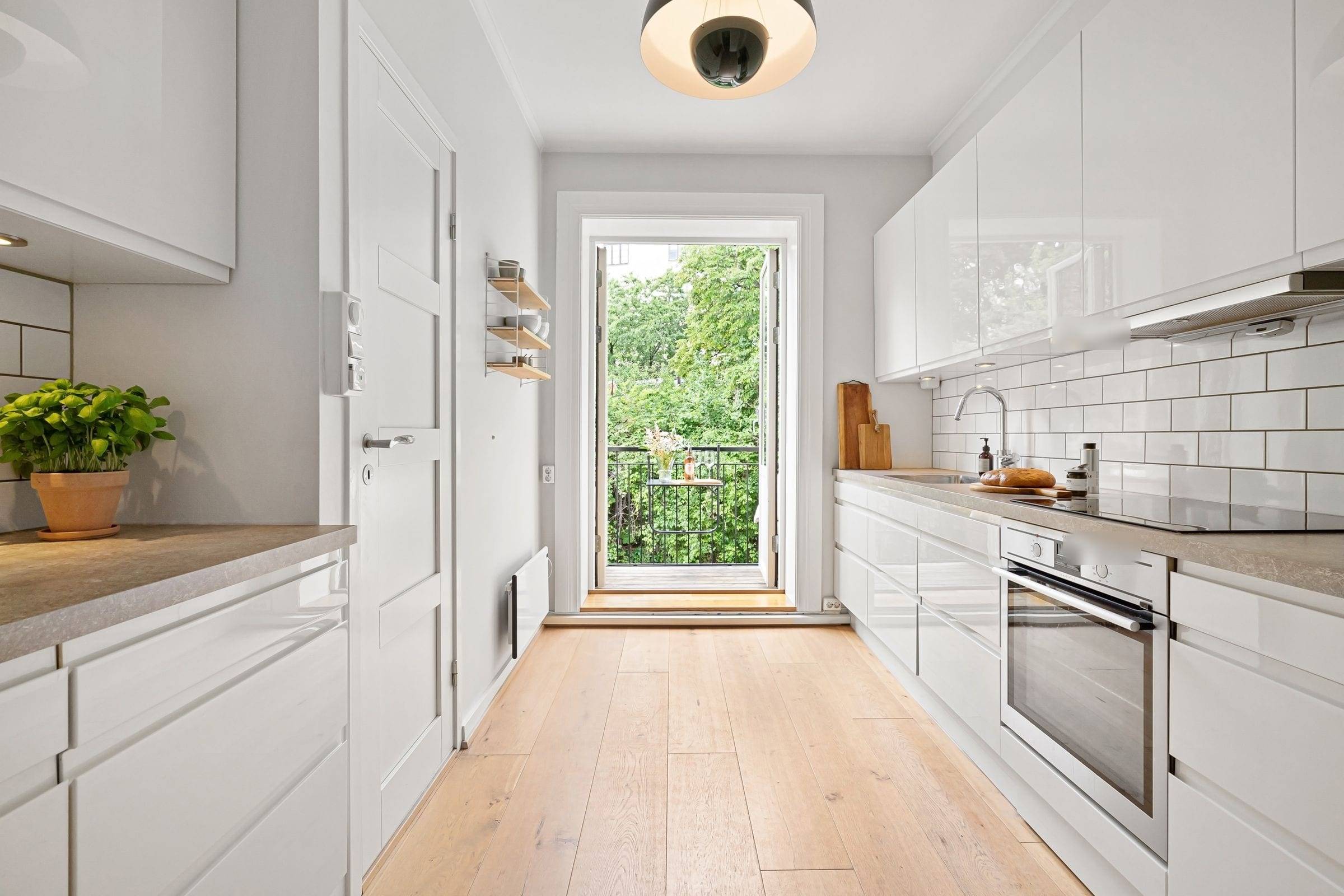 Cuisine linéaire en couloir aux façades blanches laquées sans poignée, plan effet pierre grise, porte ouverte sur un balcon